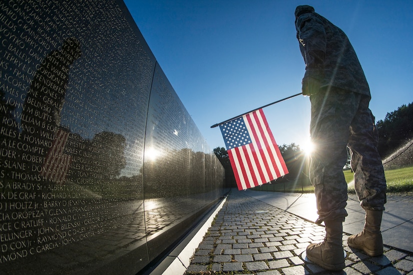 5 Facts About Veterans Day 2 Soldier stands at Vietnam War Memorial with flag.